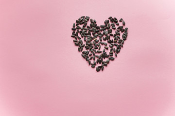 Heart laid out from black sunflower seeds on a purple background close up