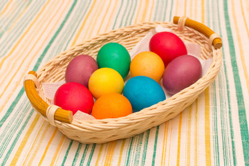 Colorful painted Easter eggs in a wicker basket on a striped tablecloth.