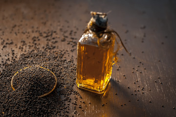 Close up of brown mustard seed,with its extracted oil on a brown wooden surface in dark Gothic...