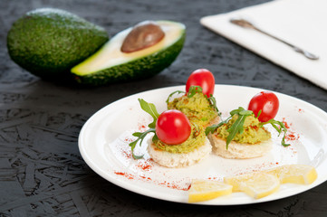 Canape with avocado and cherry tomatoes on a white plate.