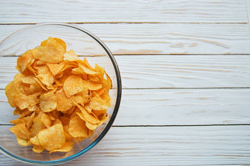 chips in a glass cup on a white wooden backdrop, harmful food