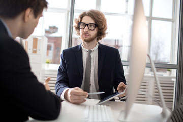 One of sales managers pointing at tablet while explaining data or making presentation to colleague