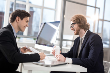 Confident agent showing his colleague curious information in business document at meeting