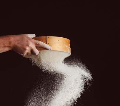 men's hands are sifting flour through a sieve on black background