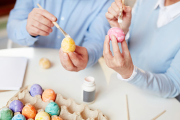 Obraz na płótnie Canvas Human hands holding eggs and paintbrushes over table and expressing their creativity for Easter festivity