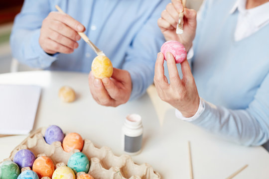 Human hands holding eggs and paintbrushes over table and expressing their creativity for Easter festivity