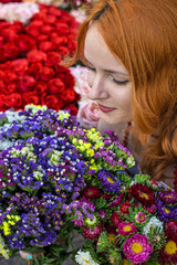 Naklejka premium Beautiful redhead Caucasian girl smelling colorful flowers in the garden 