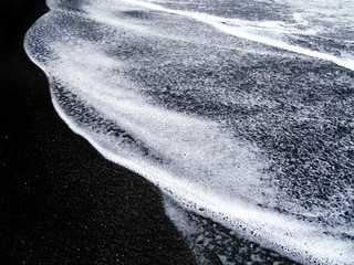 Abstract white sea foam and black sand.
Close-up view of a small smooth wave on a beach in the...
