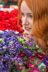 Naklejka premium Beautiful redhead Caucasian girl smelling colorful flowers in the garden 
