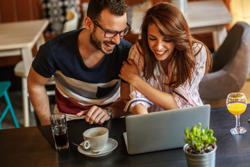 Young couple sitting at the internet cafe and relaxing on coffee break.Using laptop and free wireless.