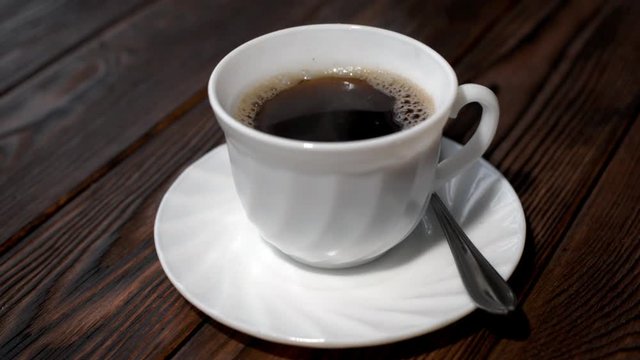 A cup of hot coffee stands on a wooden table 