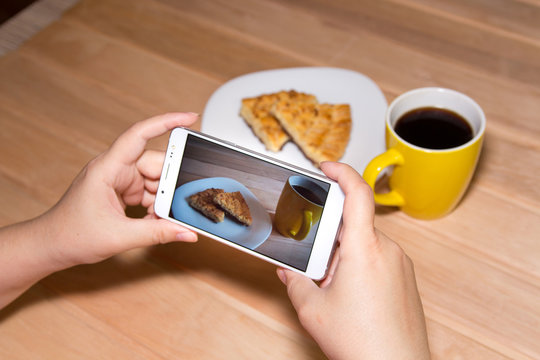 Using a mobile phone to photograph hot coffee and cookies on a wooden background with copy space. Photos of drinks and food for advertising or social media. Template.