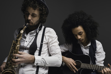 duet of musicians playing sax and guitar on black