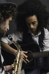 Fototapeta na wymiar young duet of musicians playing sax and acoustic guitar on black