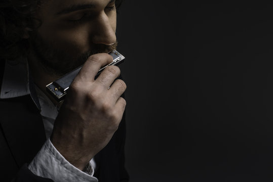 close-up portrait of handsome musician playing harmonica on black