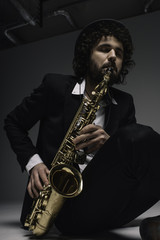Fototapeta na wymiar artistic musician playing saxophone while sitting on floor