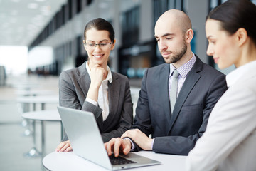 Fototapeta premium Confident business partners in formalwear sitting by table in airport lounge and browsing in the net