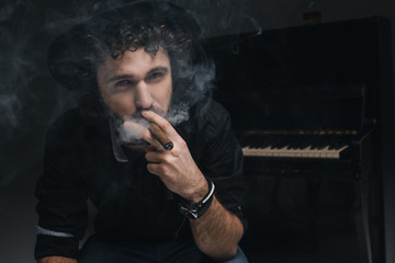 handsome musician smoking cigar in front of piano on black