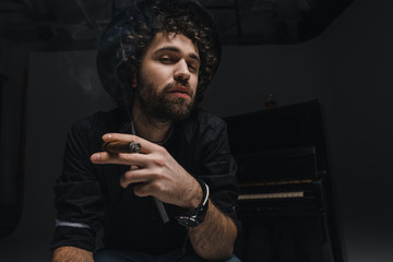 serious musician smoking cigar in front of piano on black