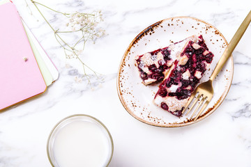 Homemade berries sponge cake slices served on white plate, cup of milk and white flowers on grey marble table. Summer breakfast. Selective focus 