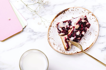 Homemade berries sponge cake slices served on white plate, cup of milk and white flowers on grey marble table. Summer breakfast. Selective focus 
