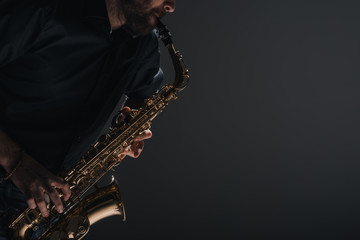 Fototapeta na wymiar cropped shot of jazzman playing saxophone on black