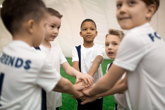 Little soccer players in uniform making pile of hands to express teambuilding