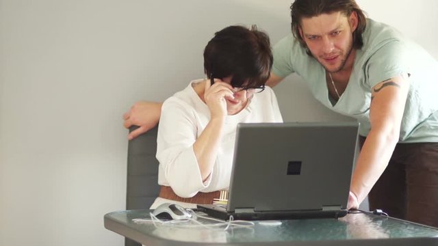 The female headmistress, the head with the young assistant discuss the details of the work process. Discussion takes place in the office near the work laptop