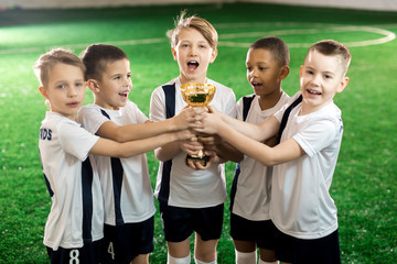 Team of little winners showing golden award after successful game in football championship