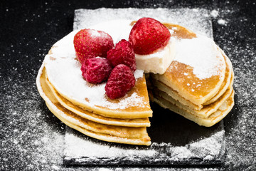 Pancakes with berries and sugar on dark background