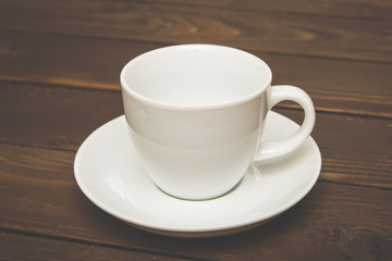 Empty white Cup with saucer on a wooden background , special toning . Crockery for coffee and tea . Template for advertising and multimedia.