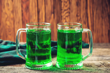 Two mug of green beer on rustic wooden background.