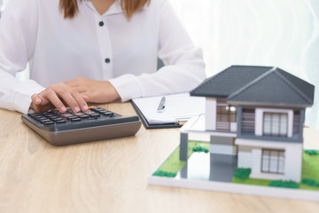 Woman calculating about installment price with estate loan agreement document and home model.