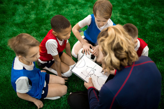 Football instructor drawing scheme of moving during soccer game or training and explaining it to group of boys © pressmaster