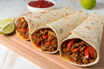 Tasty homemade burrito with vegetables and beef on wooden background.