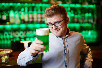 Contemporary young man making toast with glass of green beer in bar