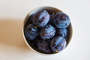 Closeup of a bowl of ripe plums on a white background. Shallow depth of focus. Health concept from nature. Copy space.