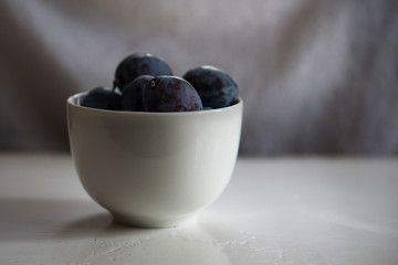 Closeup of a bowl of ripe plums on a white background. Shallow depth of focus. Health concept from nature. Copy space.