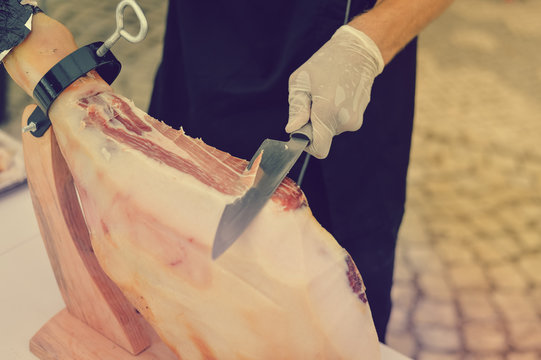 Prosciutto or jamon serrano. Close up on hands of a chef cutting traditional Italian Spanish ham. Slicing prepared hamon gastronomy background