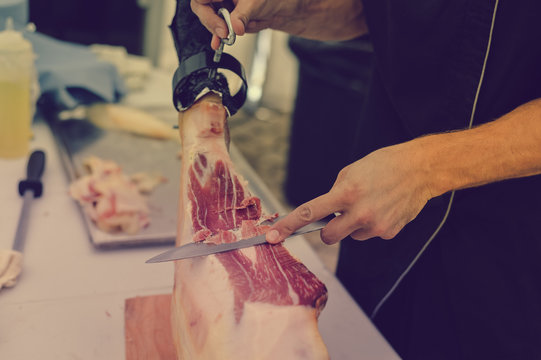 Prosciutto or jamon serrano. Close up on hands of a chef cutting traditional Italian Spanish ham. Slicing prepared hamon gastronomy background
