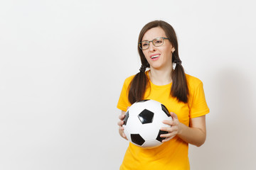 European young sad upset woman, two fun pony tails, football fan or player in glasses, yellow uniform hold classic soccer ball isolated on white background. Sport, play, football, healthy lifestyle
