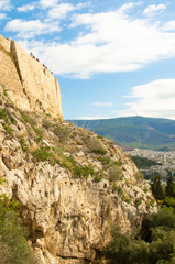 Bottom view on the wall of the Acropolis and tourists on it against the blue sky, Athens, Greece.
