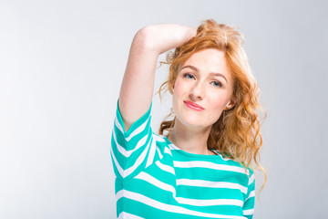 Close-up portrait of a young, beautiful woman with red curly hair in a summer dress with strips of blue in the studio on a gray background. Theme of summer vacation, tourism and summer clothes