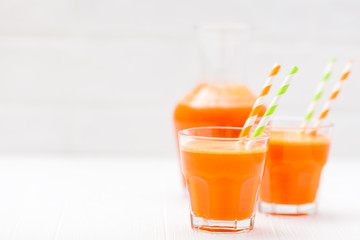 Carrot juice in beautiful glasses, cut orange vegetables and green parsley on white wooden background. Fresh orange drink. Close up photography. Selective focus. Horizontal banner