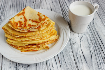 Pancakes on a white plate with honey and a cup of milk. Tasty breakfast.