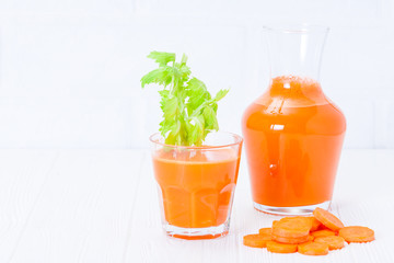 Carrot juice in beautiful glasses, cut orange vegetables and green parsley on white wooden background. Fresh orange drink. Close up photography. Selective focus. Horizontal banner