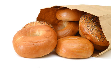 Closeup of bagels in a brown paper bag laying on its side. Horizontal format on white with reflection.