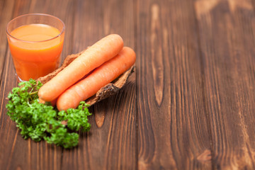 Carrot juice in beautiful glasses, cut orange vegetables and green parsley on dark brown wooden background. Fresh orange drink. Dark mood. Close up photography. Selective focus. Horizontal banner