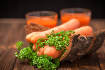 Carrot juice in beautiful glasses, cut orange vegetables and green parsley on dark brown wooden background. Fresh orange drink. Dark mood. Close up photography. Selective focus. Horizontal banner