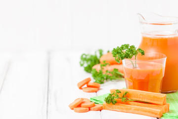Carrot juice in beautiful glasses, cut orange vegetables and green parsley on white wooden background. Fresh orange drink. Close up photography. Selective focus. Horizontal banner